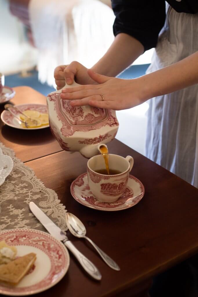 Domestic servant pouring tea into china cup.